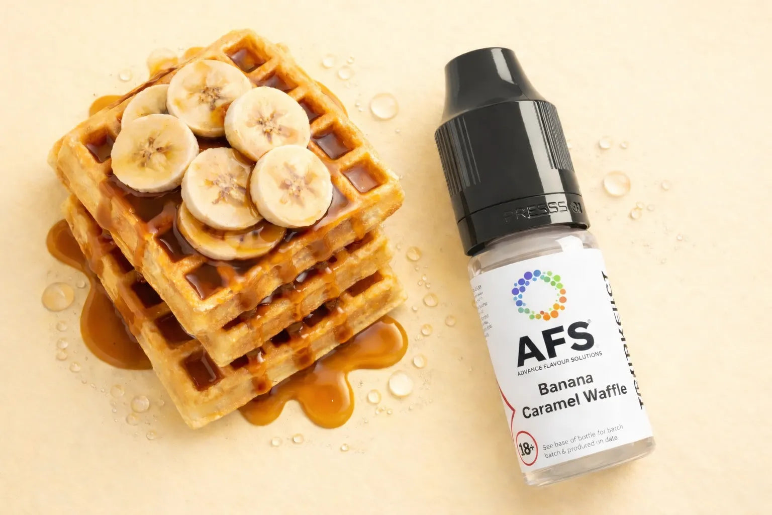 Bottle of AFS Banana Caramel Waffle vape juice next to a stack of waffles with banana slices on a beige background