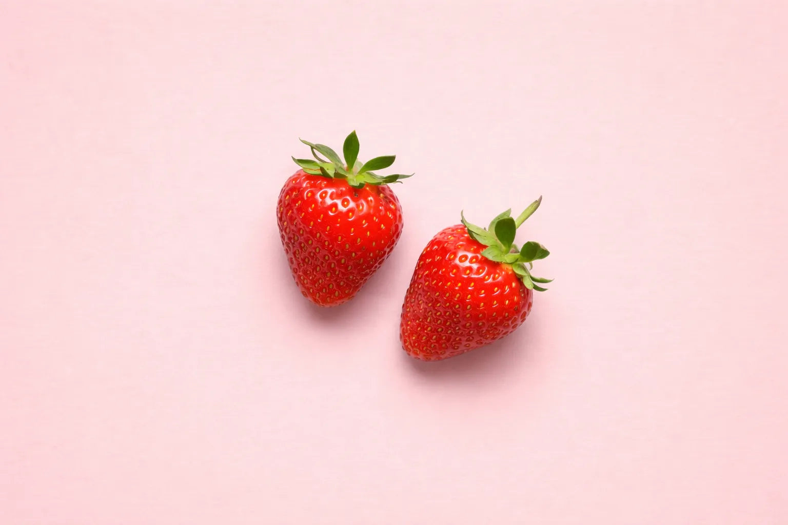 Two strawberries on a pink background
